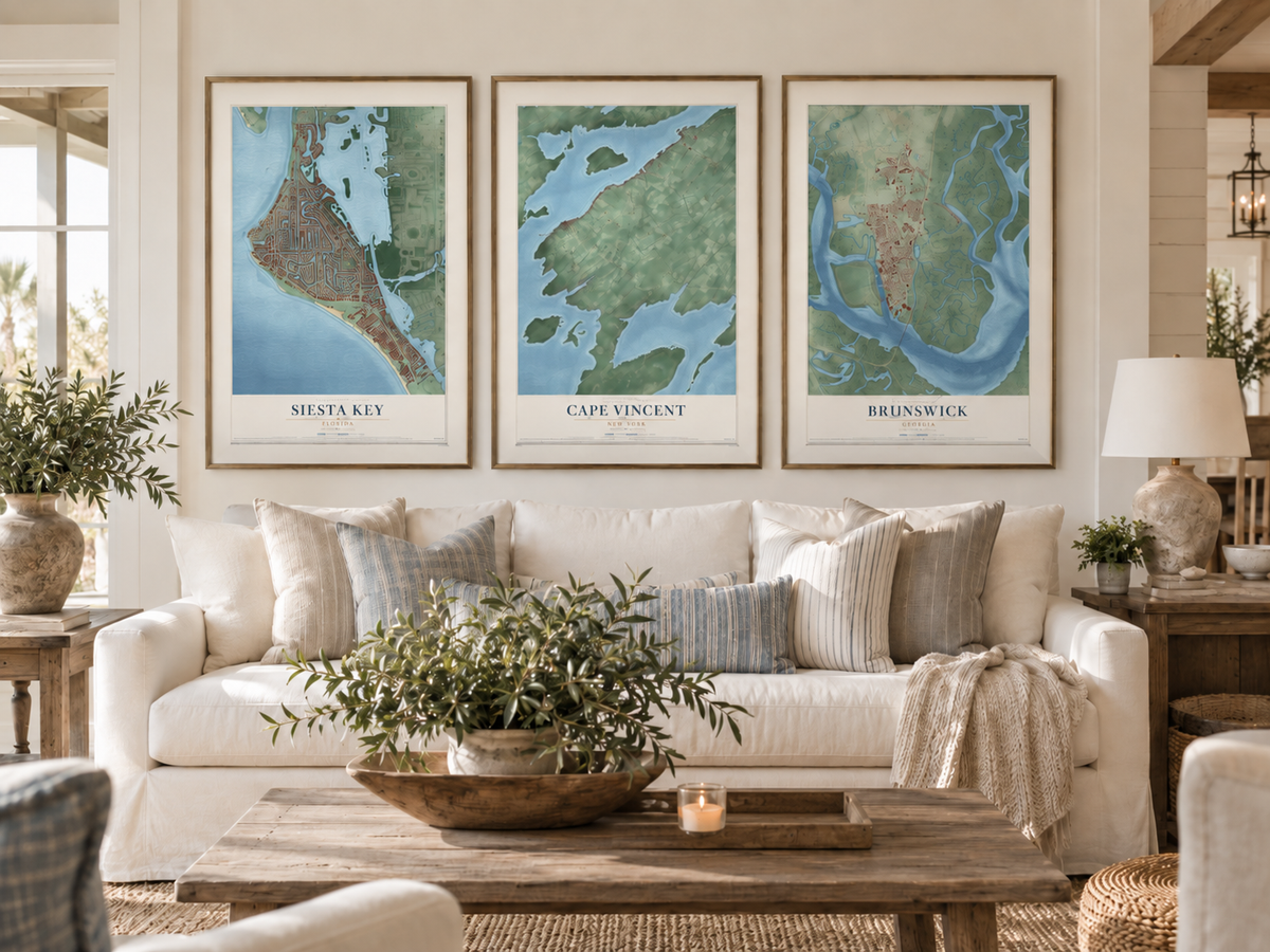 Framed maps of Siesta Key, Florida; Cape Vincent, New York; and Brunswick, Georgia, displayed above a cream sofa in a sunlit living room.